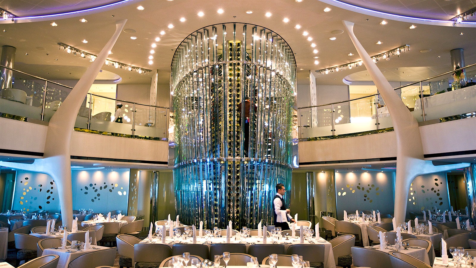 The glass wine-bottle tower in a restaurant on a Celebrity Cruise ship, with white, modern-design accents and a second tier one floor above
